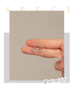 Detail shot of heart-shaped hollow earrings held by fingers showing actual scale and size