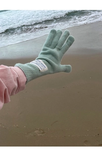 Close-up of mint green wool knit glove with white fabric label on a beach background