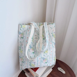 Dettaglio della borsa tote in tela a fiori con strisce blu chiaro e manici in tessuto bianco