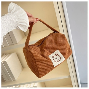 Detail of a brown corduroy square handbag with a cute cartoon bear label and zipper closure