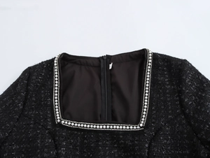 Detail des eckigen Ausschnitts mit Perlen und Metallkette am schwarzen Tweedkleid