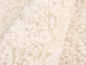 Close-up of curly faux fur texture in cream white with a matching round button detail