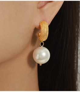 Close-up of golden C-shaped chain texture earrings with a large white pearl pendant