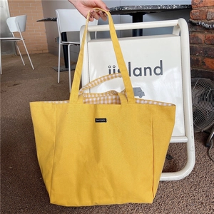 Detail of yellow canvas tote bag with check pattern lining and merciparis label on the front
