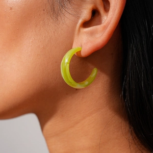 Close-up of C-shaped acrylic earring in lime green with marble texture on ear