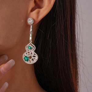 Détail de boucles d'oreilles gourde argentées avec pierres vertes sur un mannequin