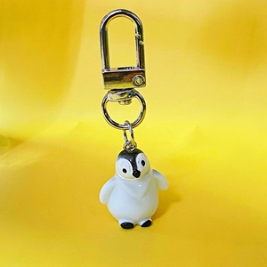 Detail of cute 3D resin penguin keychain with silver metal clip on a yellow background