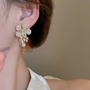 Macro shot of gold floral earrings with crystal petals and dangling pearl tassels on model