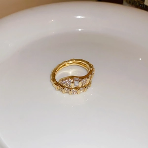 Dettaglio di un anello a serpente dorato con zirconi bianchi su un piatto bianco