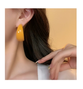 Close-up of a woman wearing yellow acrylic C-shaped hoop earrings in a retro fashion style