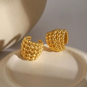 Macro detail of gold 18k plated honeycomb bead earrings on a white ceramic plate