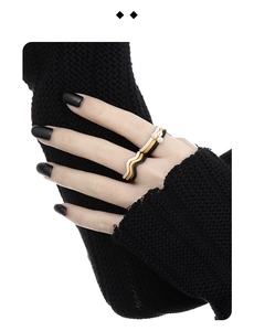 Close-up of stacked wavy metal rings in gold, silver, and black with pearl accent