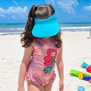 Close-up of baby sun hat with wide brim and cartoon mermaid swimsuit on a sunny beach
