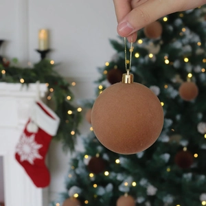 Brown velvet Christmas ball ornament with gold string held against festive decor