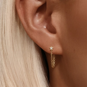 Detail showing a gold star earring with clear zircon and delicate hanging metal chains