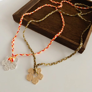 Detailed view of handmade floral pendants in gold and silver on woven cords in a wood tray