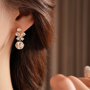 Détail de boucles d'oreilles papillon dorées avec pendentif cristal porté par le mannequin