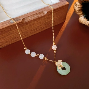 Gold-plated ginkgo leaf necklace with green Ping'an buckle on a wooden surface