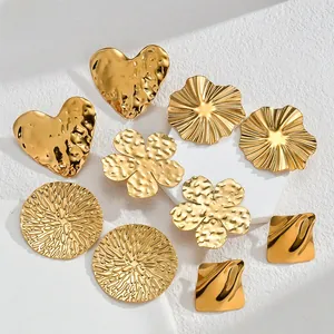 Dettaglio di orecchini dorati martellati a forma di cuore e fiore su pietra bianca