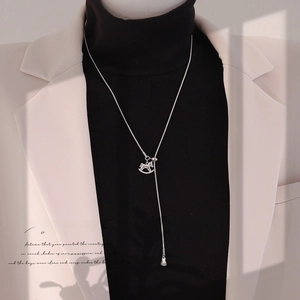 Detail of silver Y-shaped necklace with rocking horse pendant on a beige suit