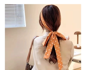 Detail of orange hair scarf with white polka dots tied in a bow on a ponytail