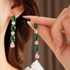 Détail de longues boucles d'oreilles pompons argentées avec zircons verts sur mannequin