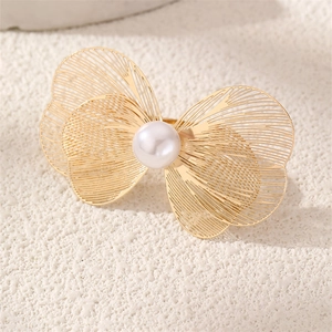 Close-up of golden hollow butterfly ring with a central white pearl on stone texture