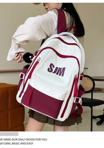 Detail of white and burgundy retro school backpack with SJM logo and black pompom charm