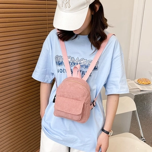 Detail shot of a minimalist pink corduroy mini backpack worn by a model in a casual setting