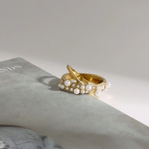 Détail d'une bague plaquée or avec perles et strass sur un fond gris élégant