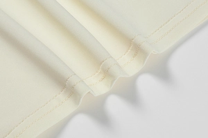 Detailed macro view of cream knitted dress hem featuring high-quality double-needle stitching