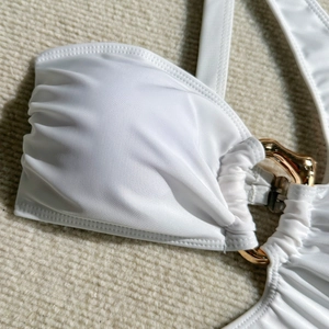 Macro detail of white pleated bikini fabric with a chunky decorative gold metal ring