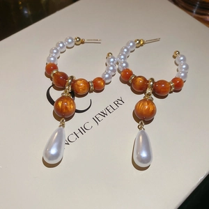 Macro detail of teardrop pearl earring with amber resin beads on a jewelry display box