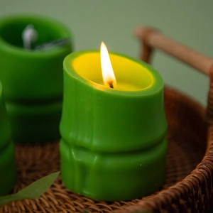 Close-up of bamboo-shaped green scented candle burning on a natural rattan tray
