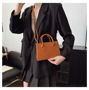 Lifestyle shot of a modern brown leather handbag held by a model in a professional blazer