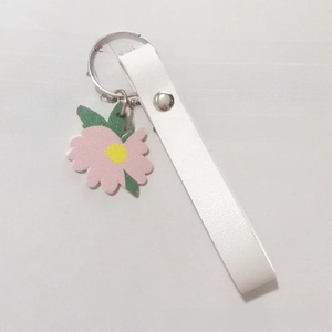 Detail of white leather keychain strap featuring a pink flower pendant on a book page