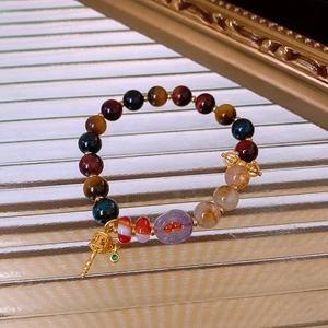 Detail of beaded gemstone bracelet with tiger eye agate and golden prayer wheel charm