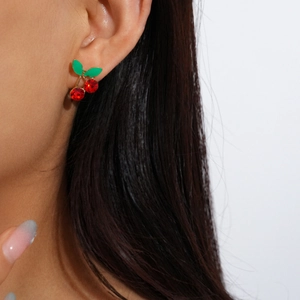 Close-up of model wearing vibrant red cherry earrings with green enamel leaves