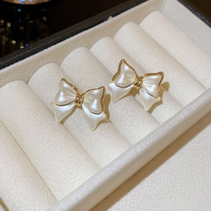 Detailed view of bow earrings with pearl white coating and gold edges in a white jewelry box