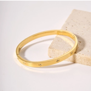 Detail of 18k gold plated stainless steel bangle with sun and star pattern on travertine