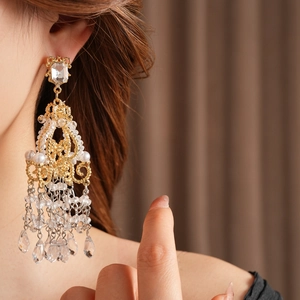 Close-up of golden chandelier earrings with crystals and pearls worn by a model