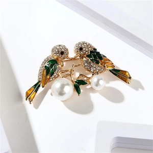 Close-up of enamel magpie bird brooch with green feathers and white pearls on gold branch
