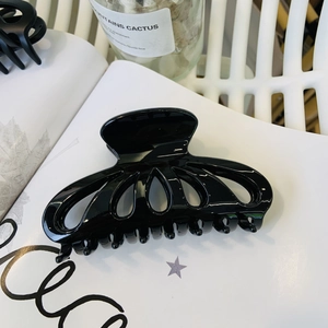 Close-up of a large black hollow flower petal hair claw clip on a white lifestyle background