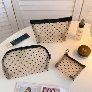 Three sizes of black mesh makeup bags with heart patterns on a minimalist table