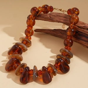 Détail de perles en acrylique ambré sur un collier vintage posé sur une branche