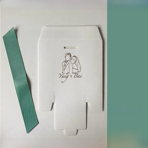 Close-up of a white wedding favor box featuring a green ribbon and a bride-groom line drawing
