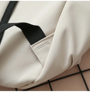 Close-up of reinforced stitching on off-white canvas backpack with black strap