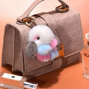 Cute mink fur bunny keychain in colorful plush hanging on a dark crocodile leather handbag