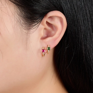 Detail von goldenen Huggie-Ohrringen mit eckigen rosa und grünen Zirkonia an einem Model
