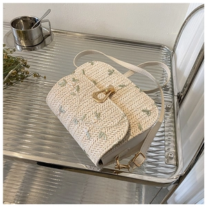 Detail of a beige woven straw bag with fine shoulder strap and elegant golden hardware